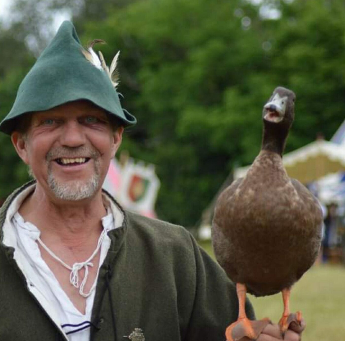 Mark smiling broadly with a brown duck perched on his hand at an outdoor event